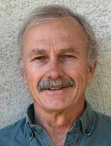 Man with mustache smiling against textured wall.