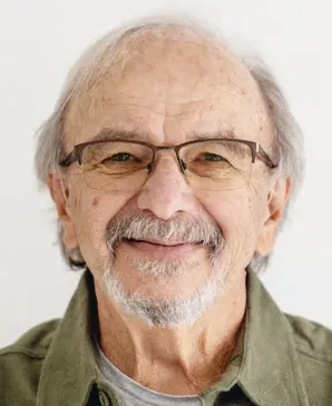 Elderly man with glasses smiling gently.