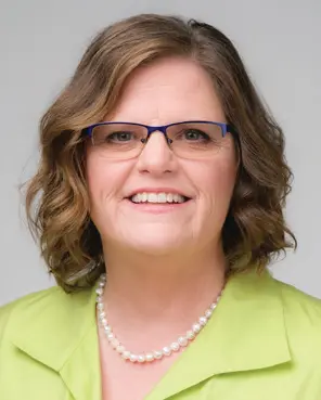 Smiling woman with glasses and pearl necklace.